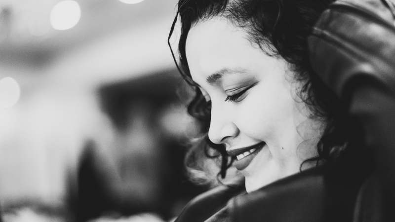 Close-up of a woman with soft, shiny perm curls smiling confidently, natural lighting, salon background